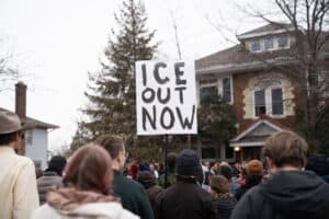 person holding sign that says, "ICE out now"